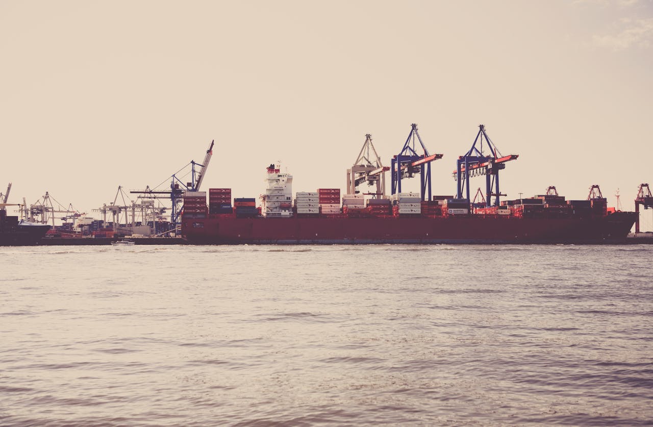 A cargo ship loaded with containers docked at a seaport under clear skies.